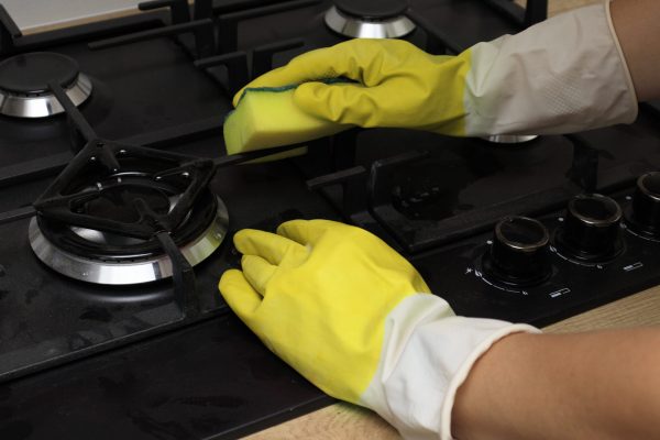 Hand in a yellow glove washes the stove. Hand washing gas stove with sponge, house cleaning concept